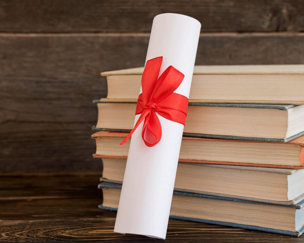 Diplôme roulé avec ruban rouge sur livres empilés