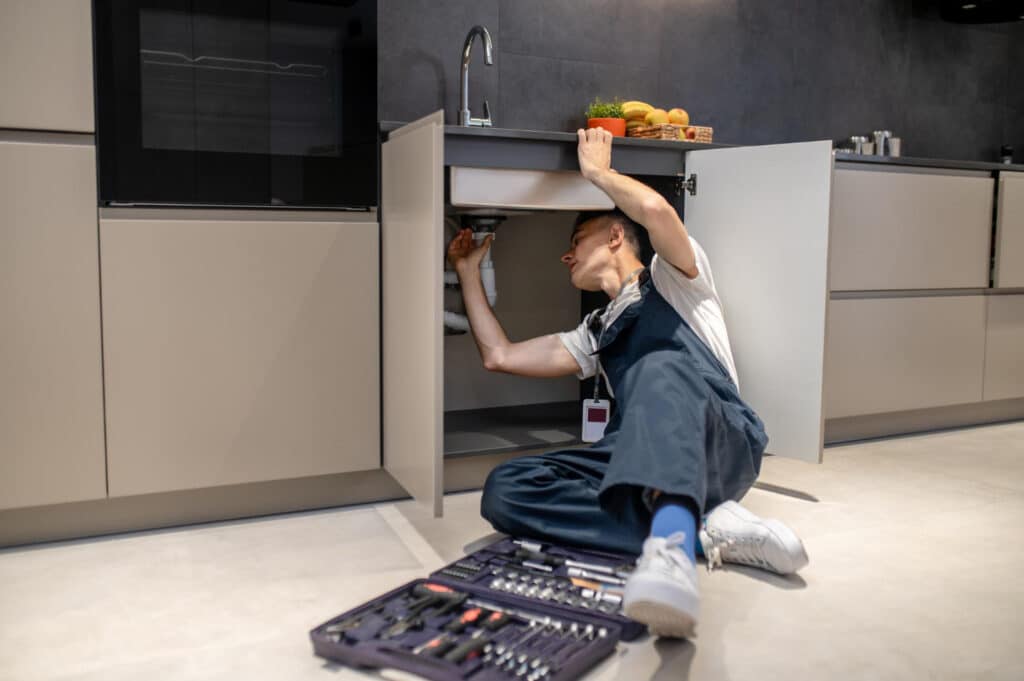 Femme réparant un évier sous meuble de cuisine