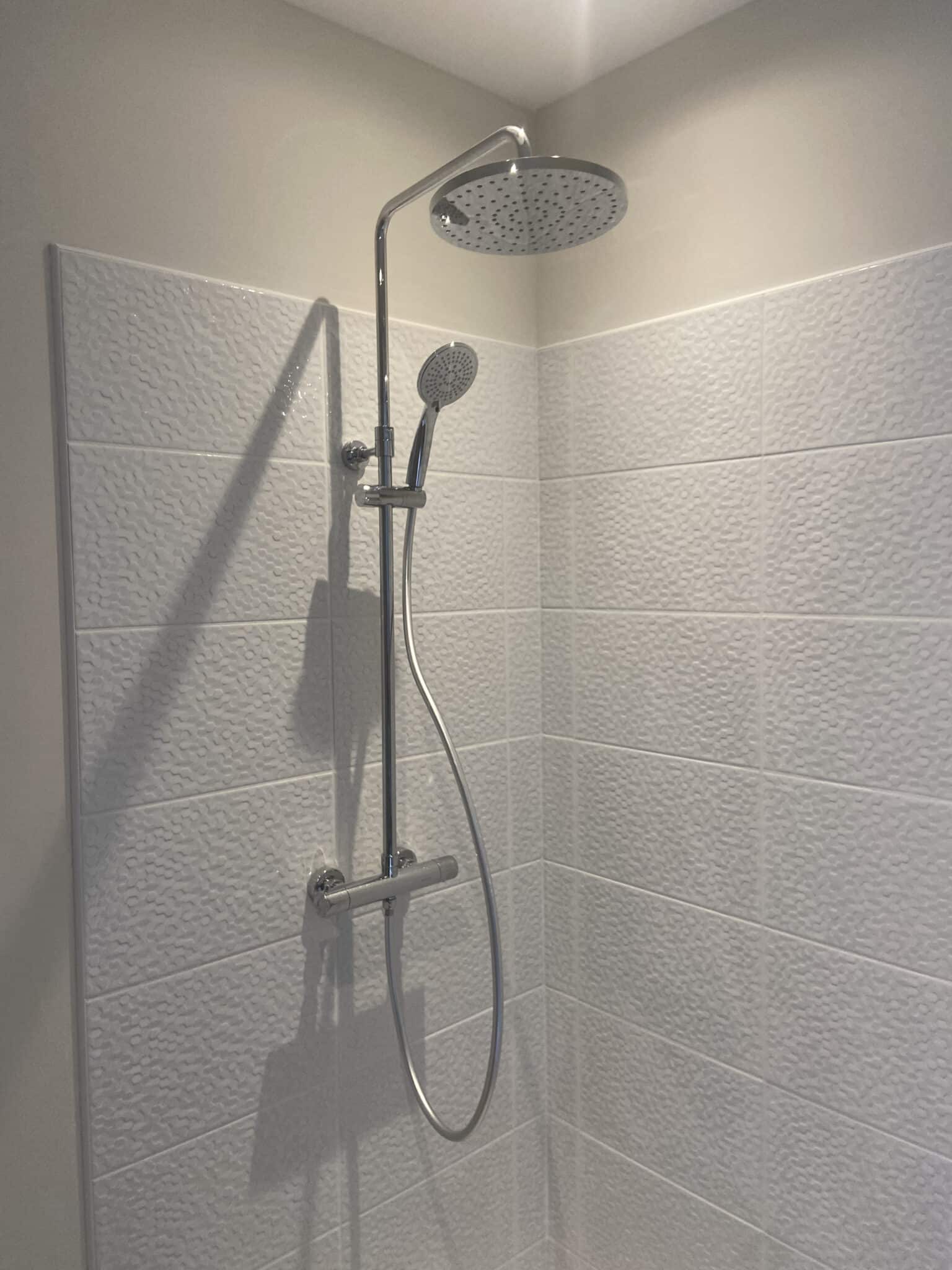 Douche avec colonne inox et carrelage mural blanc